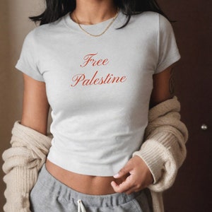 Puede incluir: Una camiseta gris con el texto "Free Palestine" en letras rojas.