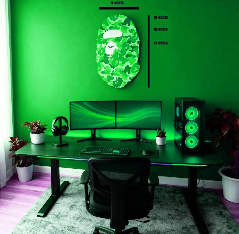 May include: A green-themed gaming setup featuring a camouflage-patterned face art piece, measuring 45.7 cm in height and 27.9 cm in width. The room includes a black desk with dual monitors, a computer tower, and a black gaming chair. The wall is painted green.