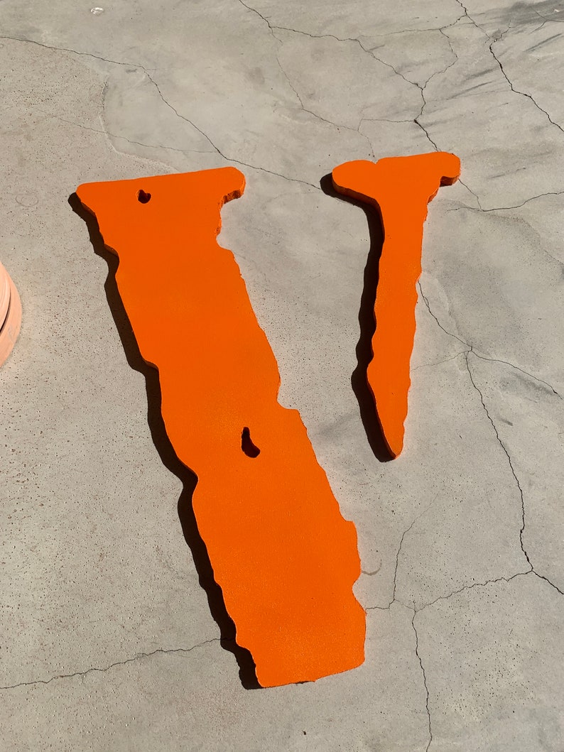 Op de afbeelding: Een oranje V-vormig bord met een ruw, getextureerd oppervlak. Het bord is gemaakt van dik materiaal en heeft een licht vervaagde uitstraling.