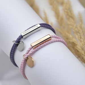 May include: Two braided leather bracelets with silver and gold accents. The purple bracelet has a silver bar with the inscription "Adam♥Sally". The pink bracelet has a gold bar and a round charm.