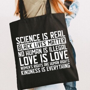 May include: Black tote bag with white text that reads "Science is real, Black Lives Matter, No Human is Illegal, Love is Love, Women's Rights are Human Rights, Kindness is Everything."