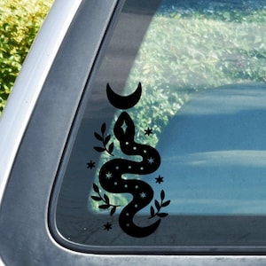 May include: Black and white car window sticker featuring a snake with stars and a crescent moon. The snake is curled up with its tail in its mouth.