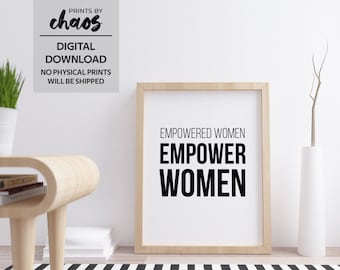 May include: A framed print with the text "EMPOWERED WOMEN EMPOWER WOMEN" in black lettering on a white background. The print is in a wooden frame and is sitting on a black and white striped rug.