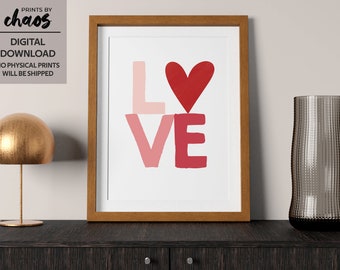 May include: A framed print with the word "LOVE" in pink and red with a red heart in the center. The print is on a dark wood surface with a gold lamp and a clear glass vase.