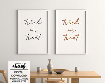 Puede incluir: Dos impresiones enmarcadas blancas con el texto "Trick or Treat" en letras negras y naranjas. Las impresiones están colgadas en una pared blanca sobre una mesa de madera con un jarrón y dos cuencos.