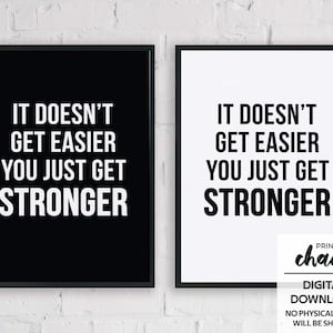 Puede incluir: Dos impresiones enmarcadas con el texto "IT DOESN'T GET EASIER YOU JUST GET STRONGER" en blanco sobre fondo negro y texto negro sobre fondo blanco. Las impresiones se muestran en una pared de ladrillos blancos.