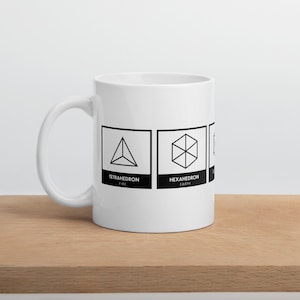 May include: White ceramic mug with black geometric shapes and text. The shapes represent the four elements: fire, earth, air, and water. The text reads "Tetrahedron Fire", "Hexahedron Earth", "Octahedron Air", and "Icosahedron Water".