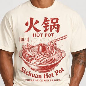 Könnte beinhalten: Ein cremefarbenes T-Shirt mit einer roten Grafik eines Sichuan-Hot-Pots, inklusive Stäbchen, Gemüse und Fleisch. Der Text lautet "火锅", "HOT POT", "四川", "Sichuan Hot Pot" und "WHERE SPICE MEETS SOUL." Das Design hat eine abgenutzte, vintage-artige Textur.
