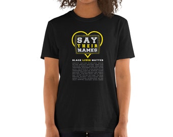 Puede incluir: Camiseta negra con el texto "SAY THEIR NAMES" en un diseño en forma de corazón amarillo. Debajo del texto está "BLACK LIVES MATTER" y una lista de nombres. La camiseta es de material suave.