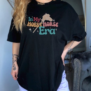 May include: Black oversized t-shirt with a graphic of a hobby horse and the text "In My Hobby Horse Era".