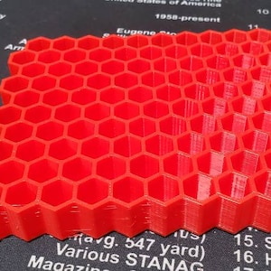May include: A red plastic honeycomb-shaped object with a textured surface. The object is made up of multiple layers of hexagons.