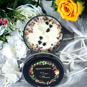 May include: A white candle with black stones and dried flowers in a black tin container. The label on the tin reads "Spiritual Kids Twin Flame".