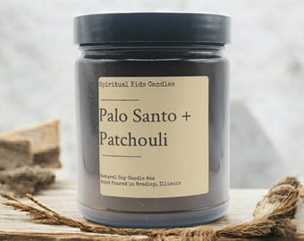 May include: A black glass candle jar with a brown label that reads "Spiritual Kids Candles Palo Santo + Patchouli Natural Soy Candle 8oz Hand Poured in Bradley, Illinois".