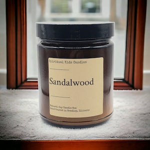 May include: A brown glass candle jar with a black lid. The label reads "Spiritual Kids Candles" and "Sandalwood". The label also says "Natural Soy Candle 8oz Hand Poured in Bradley, Illinois".