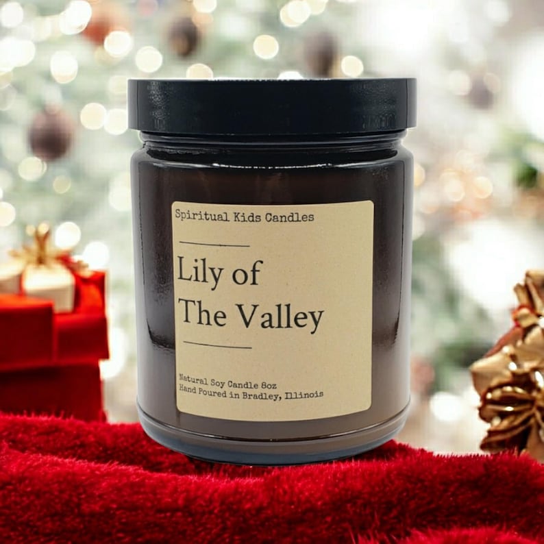 Puede incluir: Un tarro de vela de vidrio marr&oacute;n con una tapa negra. La etiqueta dice "Spiritual Kids Candles Lily of The Valley Natural Soy Candle Box Hand Poured in Bradley, Illinois".