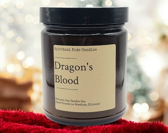 Può includere: Un barattolo di vetro marrone per candele con un coperchio nero. L'etichetta recita "Spiritual Kids Candles Dragon's Blood Natural Soy Candle 6oz Hand Poured in Bradley, Illinois."