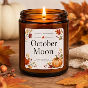 May include: A lit candle in an amber glass jar with a white label featuring the text Spiritual Kids Candles, October Moon, and Natural Soy Candle 8oz, Hand Poured in Bradley, Illinois, decorated with illustrations of autumn leaves and a pumpkin.