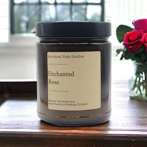 May include: A brown glass candle jar with a black lid. The label reads "Spiritual Kids Candles Enchanted Rose Natural Soy Candle 8oz Hand Poured in Bradley, Illinois."