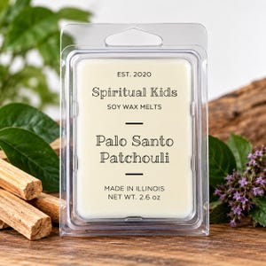 May include: A rectangular clear plastic clamshell package containing off-white soy wax melts. The label reads: EST. 2020, Spiritual Kids, SOY WAX MELTS, Palo Santo Patchouli, MADE IN ILLINOIS, NET WT. 2.6 oz. The wax is visible through the clear plastic.