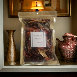 May include: A clear plastic bag filled with potpourri, labeled "Spiritual Vids Georgia Peach Potpourri". The bag is sitting on a shelf with a gold vase and a pink teapot.
