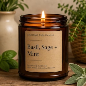 May include: A lit candle in a brown glass jar with a tan label reading Spiritual Kids Candles, Basil, Sage + Mint, Natural Soy Candle 8oz, Hand Poured in Bradley, Illinois. The candle features a single burning wick centered in the jar.
