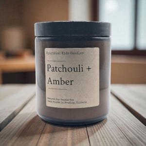 Puede incluir: Una vela en tarro de cristal marrón con tapa negra. La etiqueta dice "Spiritual Kids Candles" y "Patchouli + Amber". La vela está vertida a mano en Bradley, Illinois. La vela está sobre una superficie de madera.