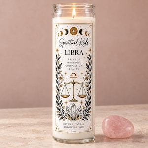 Könnte beinhalten: Eine hohe, klare Glas-Stumpenkerze mit weißem Wachs und brennendem Docht. Das Etikett zeigt goldene und schwarze himmlische Grafiken sowie den Text "Spiritual Kids LIBRA BALANCE HARMONY COMPASSION BEAUTY RITUALS FOR A BRIGHTER YOU 14 oz".