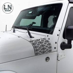 Könnte beinhalten: Ein weißer Jeep Wrangler mit schwarzen und weißen geometrischen Mustern auf den Motorhaubenabdeckungen. Der Jeep hat ein Trail Rated-Abzeichen an der Fahrertür.