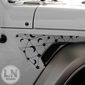May include: A gray Jeep Wrangler with a black and white geometric design on the fender. The design features stars and crescent moons.