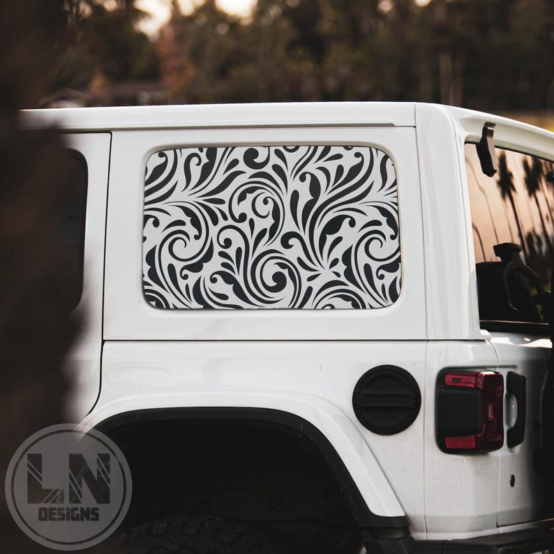 May include: A white Jeep Wrangler with a black and white floral pattern decal on the rear window. The decal is a repeating pattern of swirls and leaves.