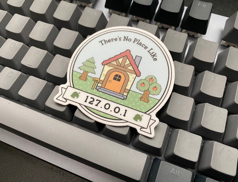 May include: A round sticker with a cartoon house, trees, and the text "There's No Place Like 127.0.0.1".