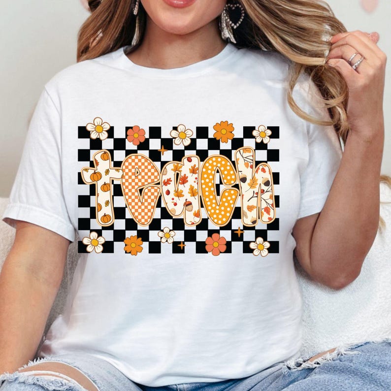 May include: White t-shirt featuring the word "TEACH" in a retro font, with fall-themed designs. The letters are decorated with pumpkins, leaves, and polka dots. The word is set against a black and white checkered background, with floral accents.