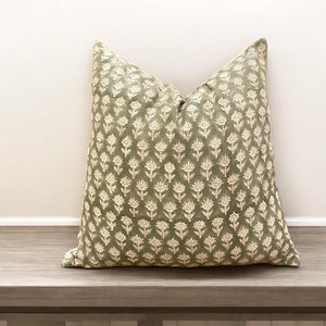 May include: A green cushion with a white floral pattern. The cushion is sitting on a wooden surface.