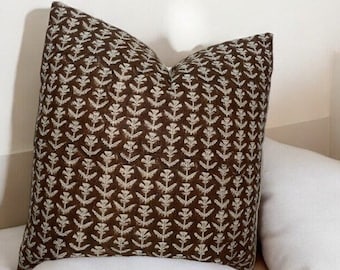 May include: A brown cushion with a white floral pattern. The cushion is sitting on a white sofa.