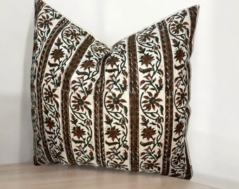 May include: A white pillow with a brown and green floral pattern. The pillow has a rectangular shape and is sitting on a light brown surface.