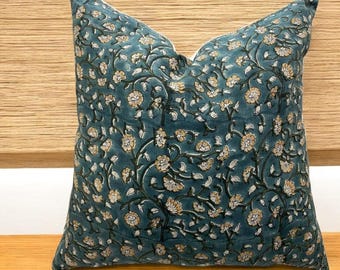 May include: A teal blue pillow with a floral pattern. The flowers are white with yellow centers and are arranged on a repeating vine pattern.