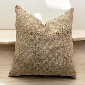 May include: A beige throw pillow with a white and brown floral pattern. The pillow is made of a soft, textured fabric.