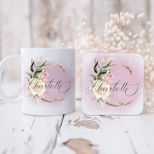 May include: White ceramic mug and matching coaster with a pink watercolor background and gold glitter accents. The mug and coaster feature a floral design with a white flower and green leaves. The name "Charlotte" is written in black cursive script.