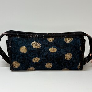 May include: A rectangular fabric pouch featuring a dark blue and black floral pattern with gold-colored flower centers. The exterior is accented by a black fabric with a copper-colored speckled design, and the bag includes a metallic zipper closure.