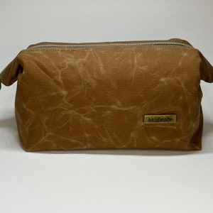 May include: A brown canvas toiletry bag with a zipper closure and a small brass tag that reads "handmade".