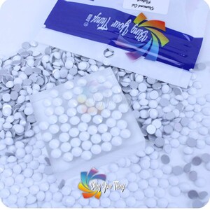 May include: A close-up of a bag of white round self-adhesive rhinestones. The bag is labeled "Bling Your Things" and "Diamond Cut".