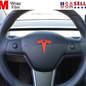 May include: A black steering wheel with a red Tesla logo in the center. The wheel has controls on either side and the word "AIRBAG" is visible at the bottom. The top left corner has the text "3M Wrap Film".