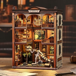 Puede incluir: Maqueta de madera detallada de un museo de fósiles, con múltiples pisos, exhibiciones, un esqueleto de dinosaurio y el texto "Fossil Museum" en la fachada. El modelo está iluminado desde el interior, mostrando los detalles.