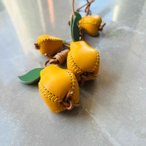 May include: A group of four yellow leather pears with green leaves attached. The pears are stitched together with a brown leather cord.