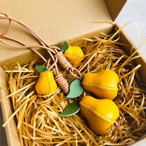 May include: A set of four yellow leather pear-shaped keychains with green leaf accents. The keychains are connected by a brown leather cord.