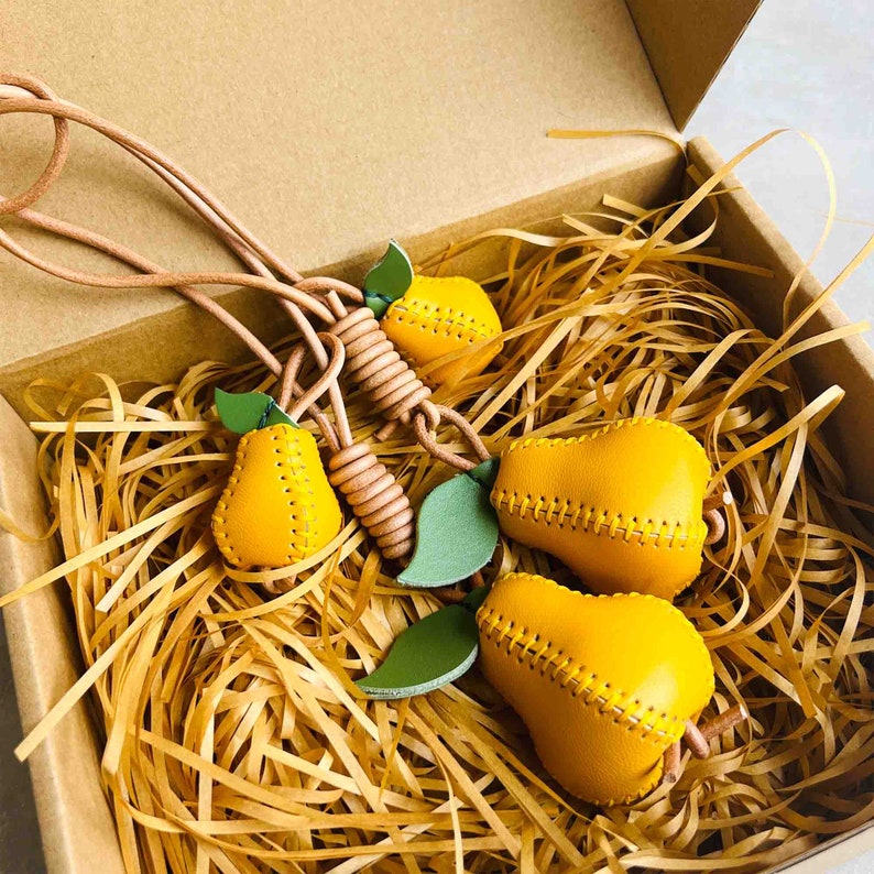 May include: A set of four yellow leather pear-shaped keychains with green leaf accents. The keychains are connected by a brown leather cord.