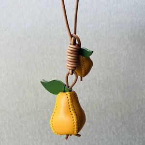 May include: A yellow leather pear charm necklace with a green leaf. The pear is stitched with a yellow thread.