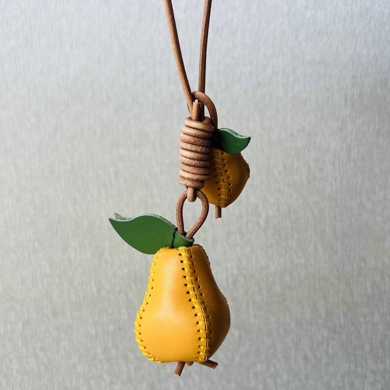 May include: A yellow leather pear charm necklace with a green leaf. The pear is stitched with a yellow thread.