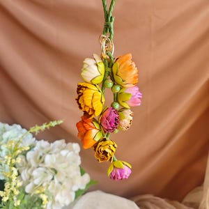 May include: A colorful leather flower keychain with a green cord and a gold clasp. The flowers are in shades of yellow, orange, pink, and white.