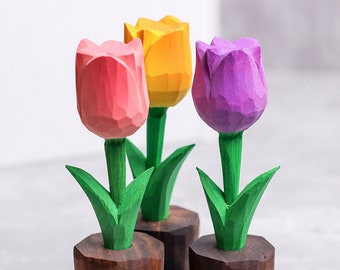 May include: Three wooden tulip sculptures in pink, yellow, and purple. Each tulip has a green stem and leaves, set in a small, dark wooden base. The carved details give a rustic, handcrafted appearance.